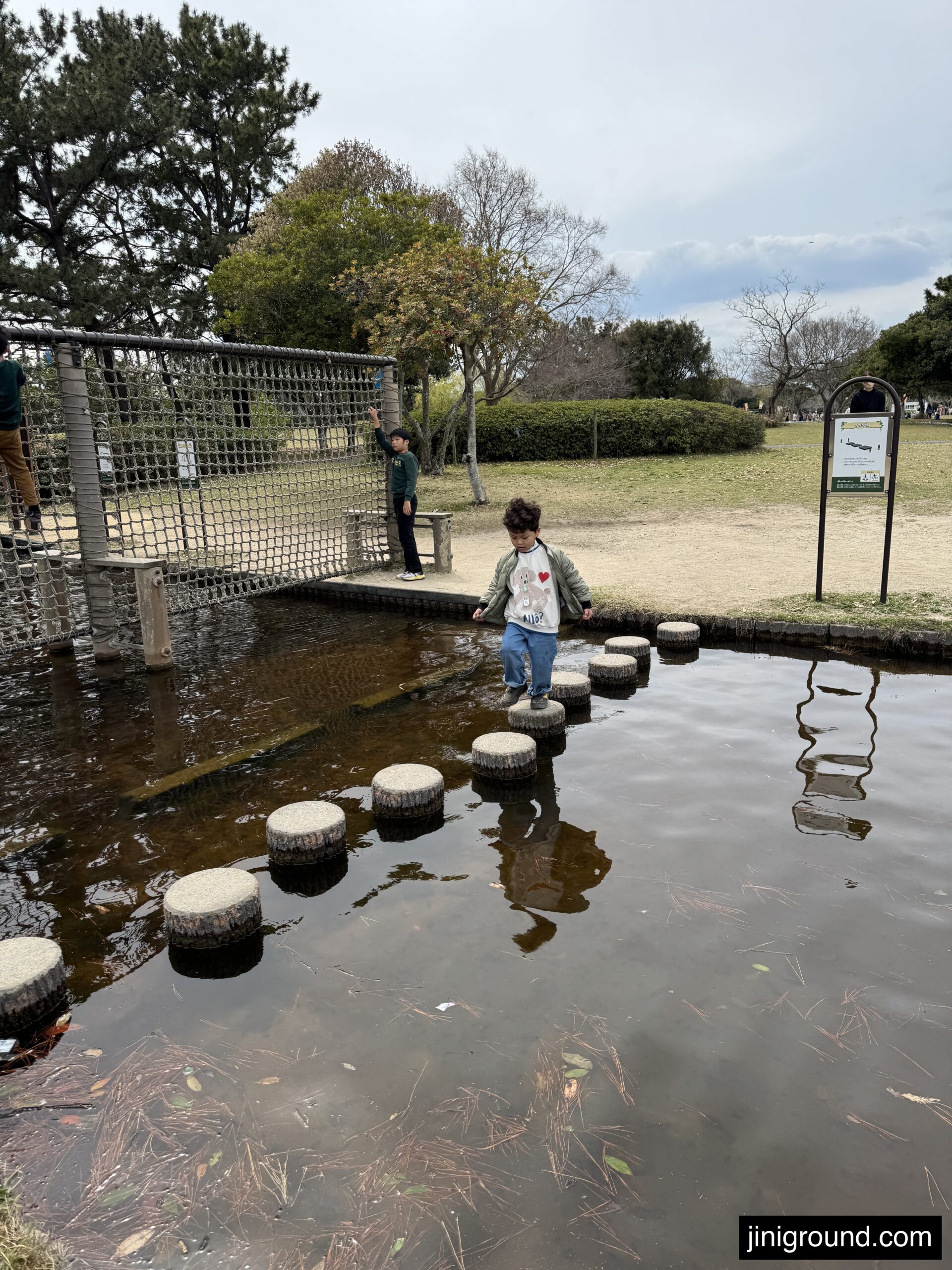 Boy carefully crossing stepping stones over pond at Uminonakamichi Seaside Park Fukuoka Japan