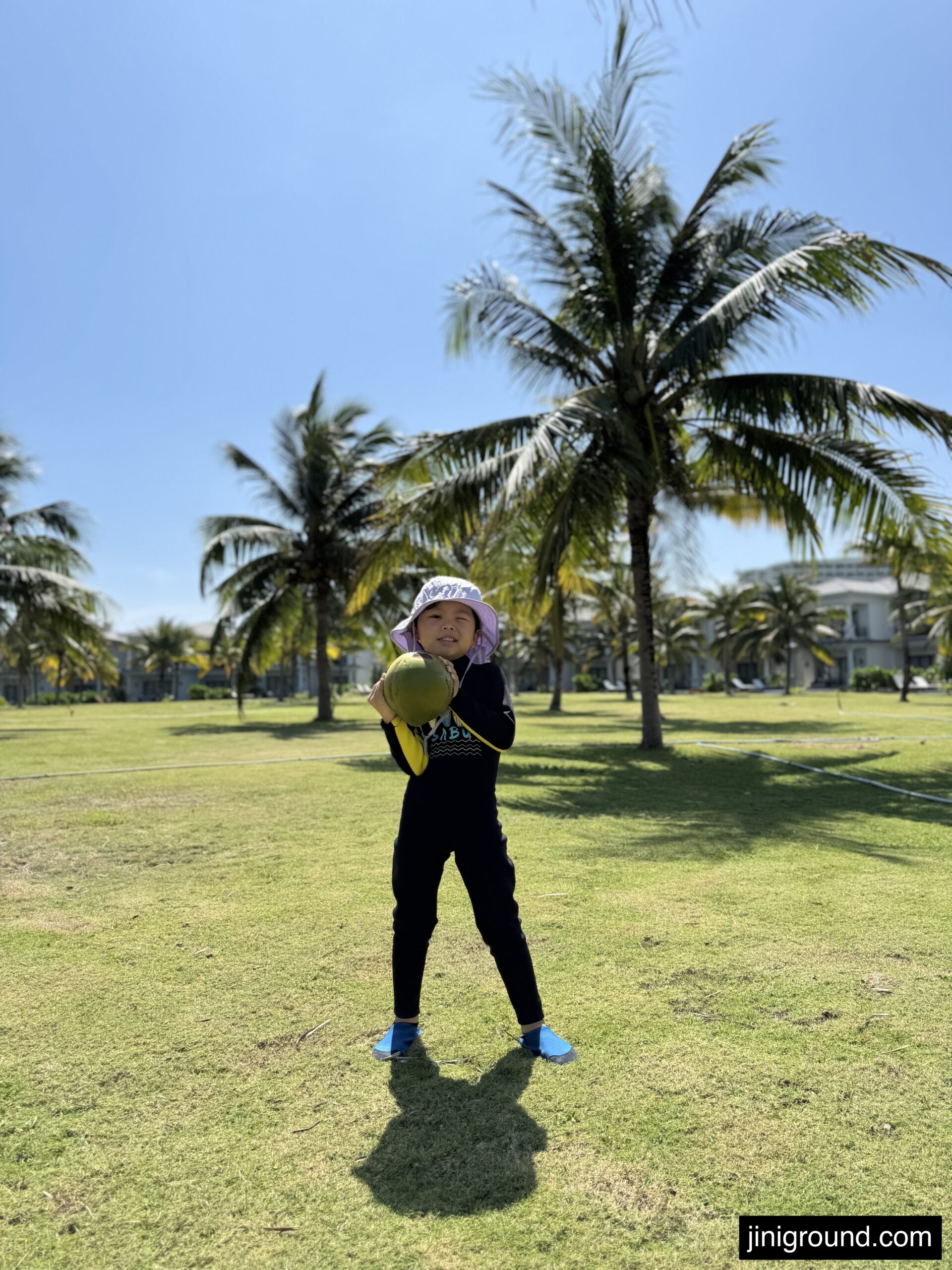 56 month old boy holding fresh coconut on green lawn with palm trees at Vinpearl Resort Nha Trang