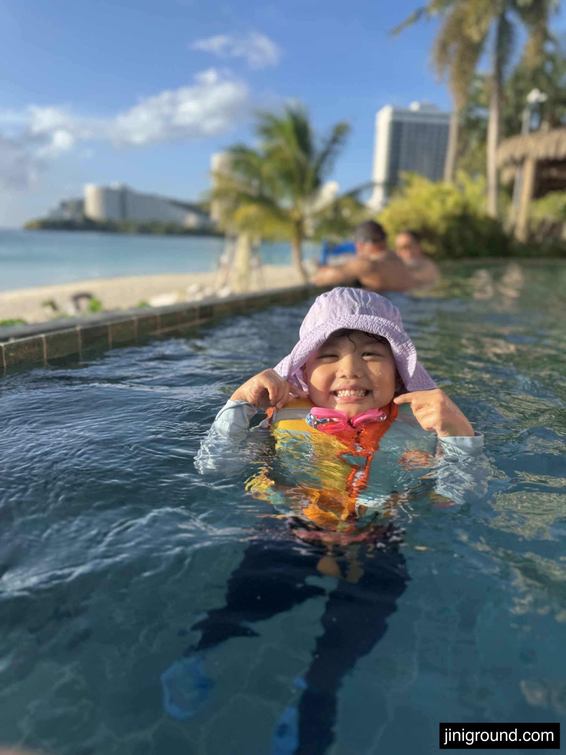 Boy smiling in infinity pool overlooking Tumon Beach and palm trees at Dusit Guam
