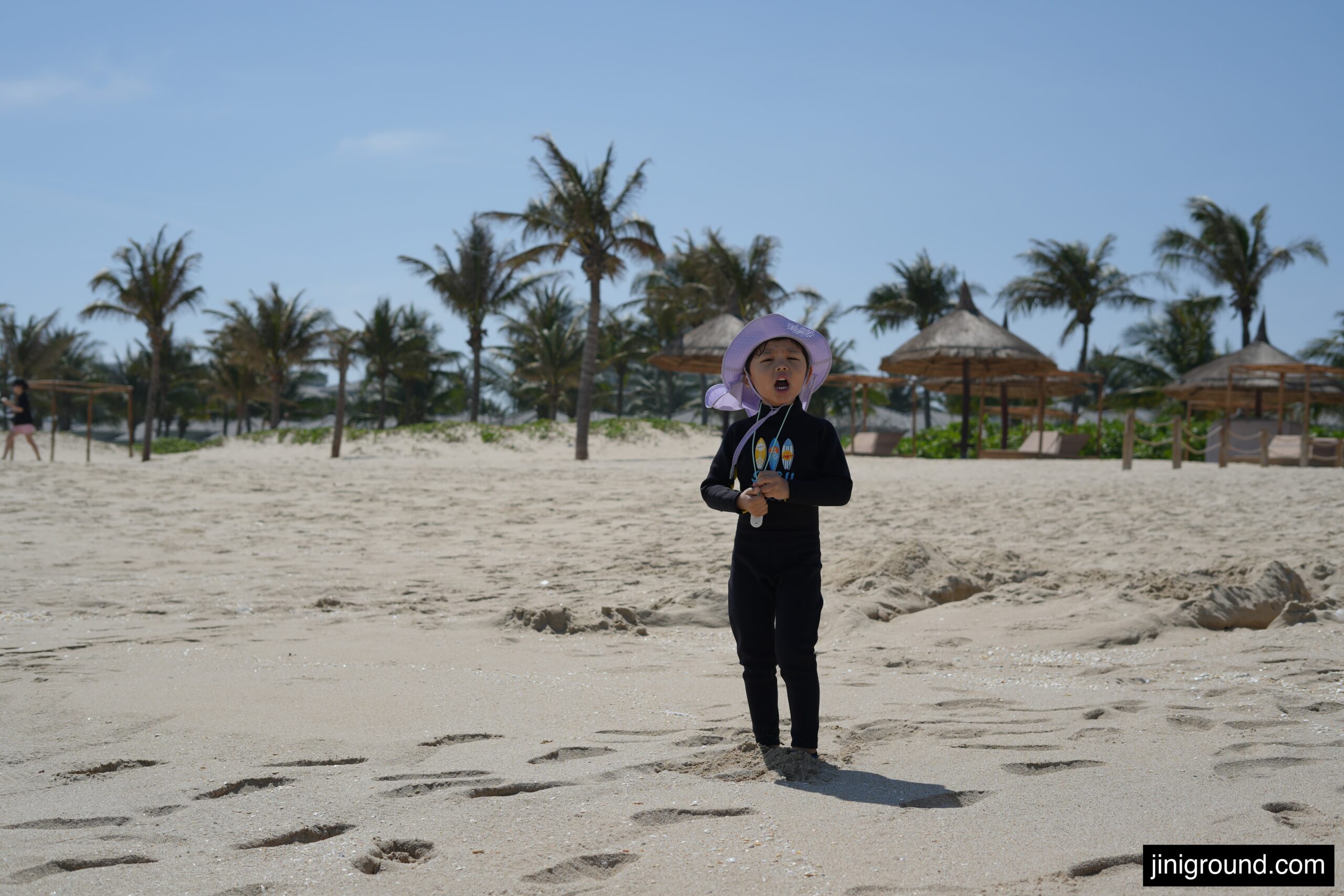 56 month old boy standing on white sand private beach with palm trees at Vinpearl Cam Ranh