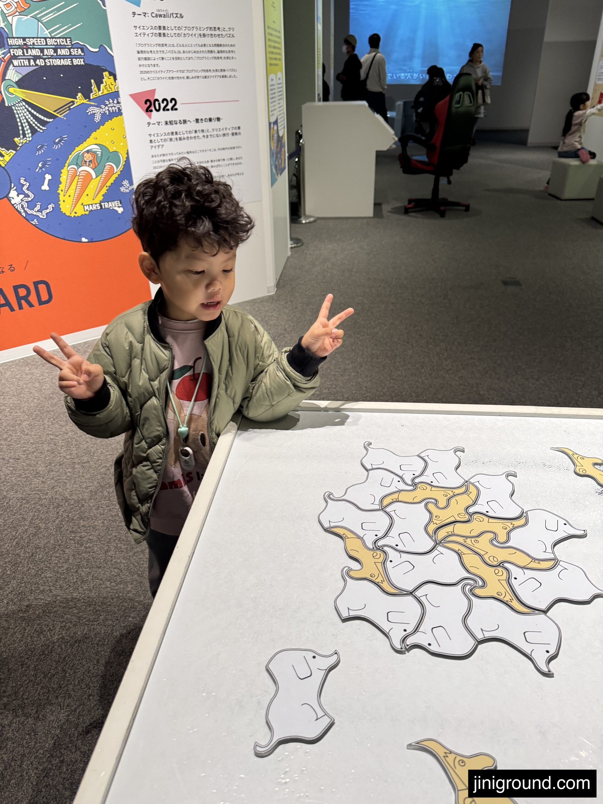 60 month old boy making peace sign next to animal shape puzzle at Fukuoka Science Museum