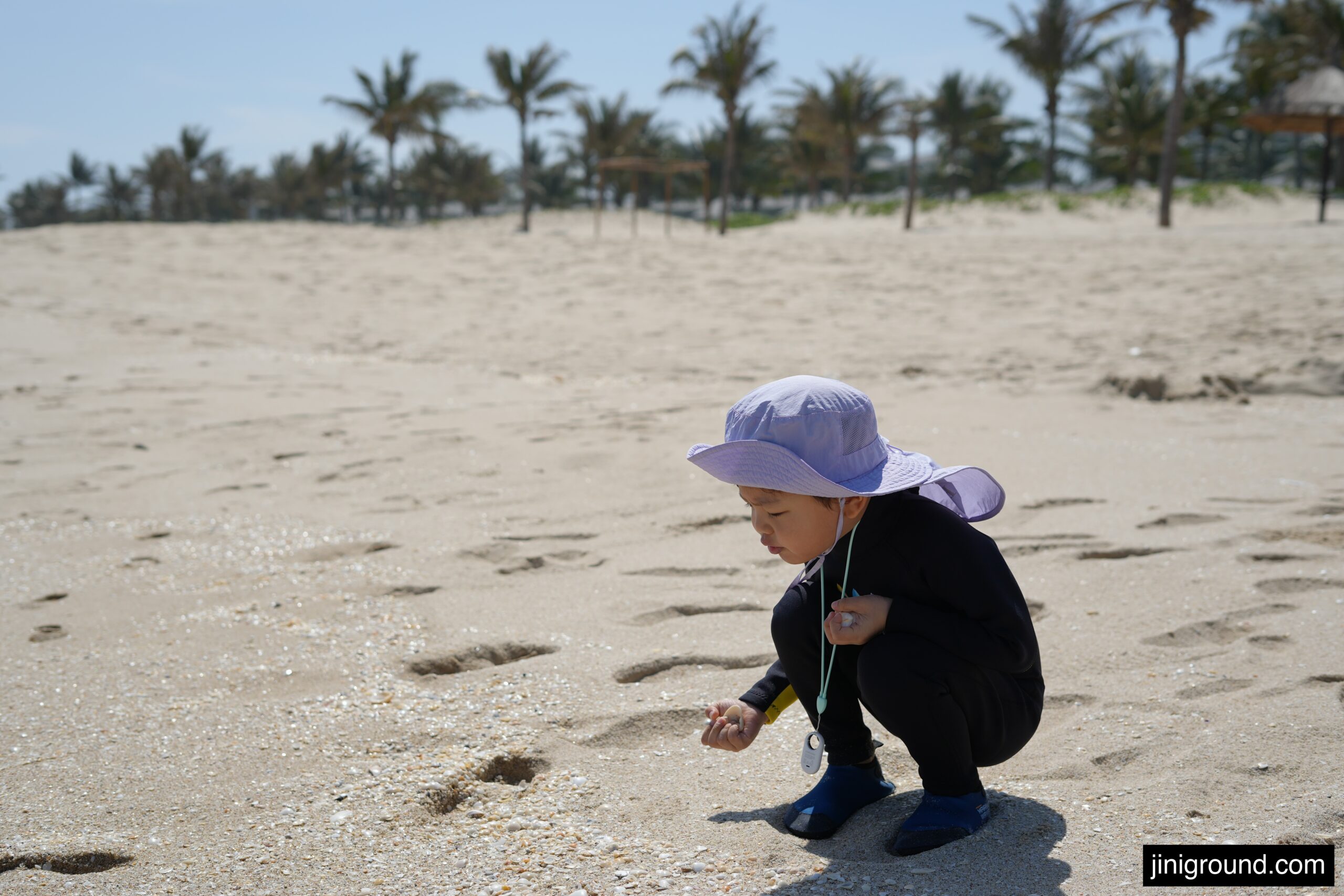 Young boy crouching on beach picking up seashells at Vinpearl Cam Ranh Nha Trang Vietnam