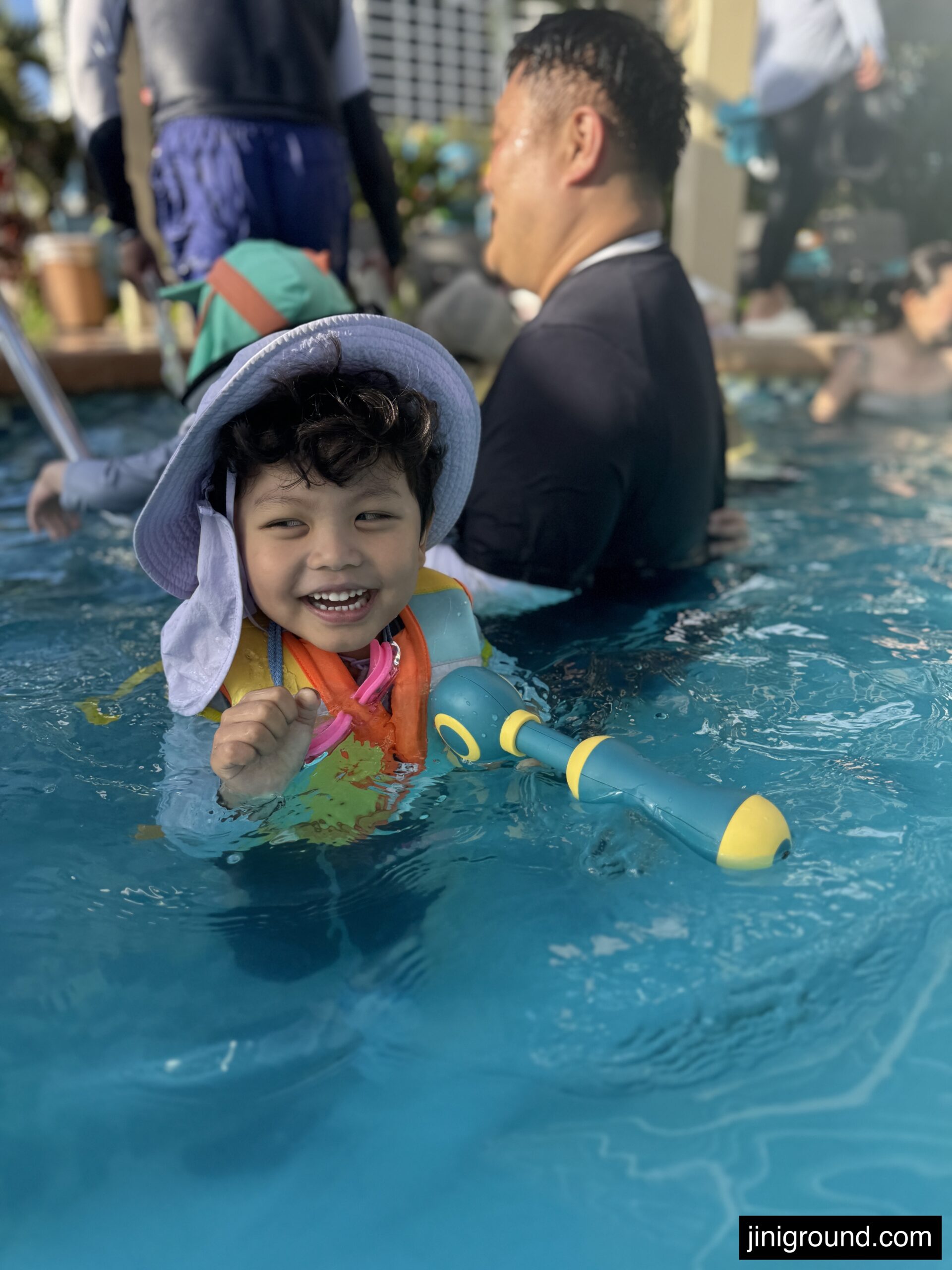 Happy boy with sun hat smiling in swimming pool with dad at Dusit Guam resort
