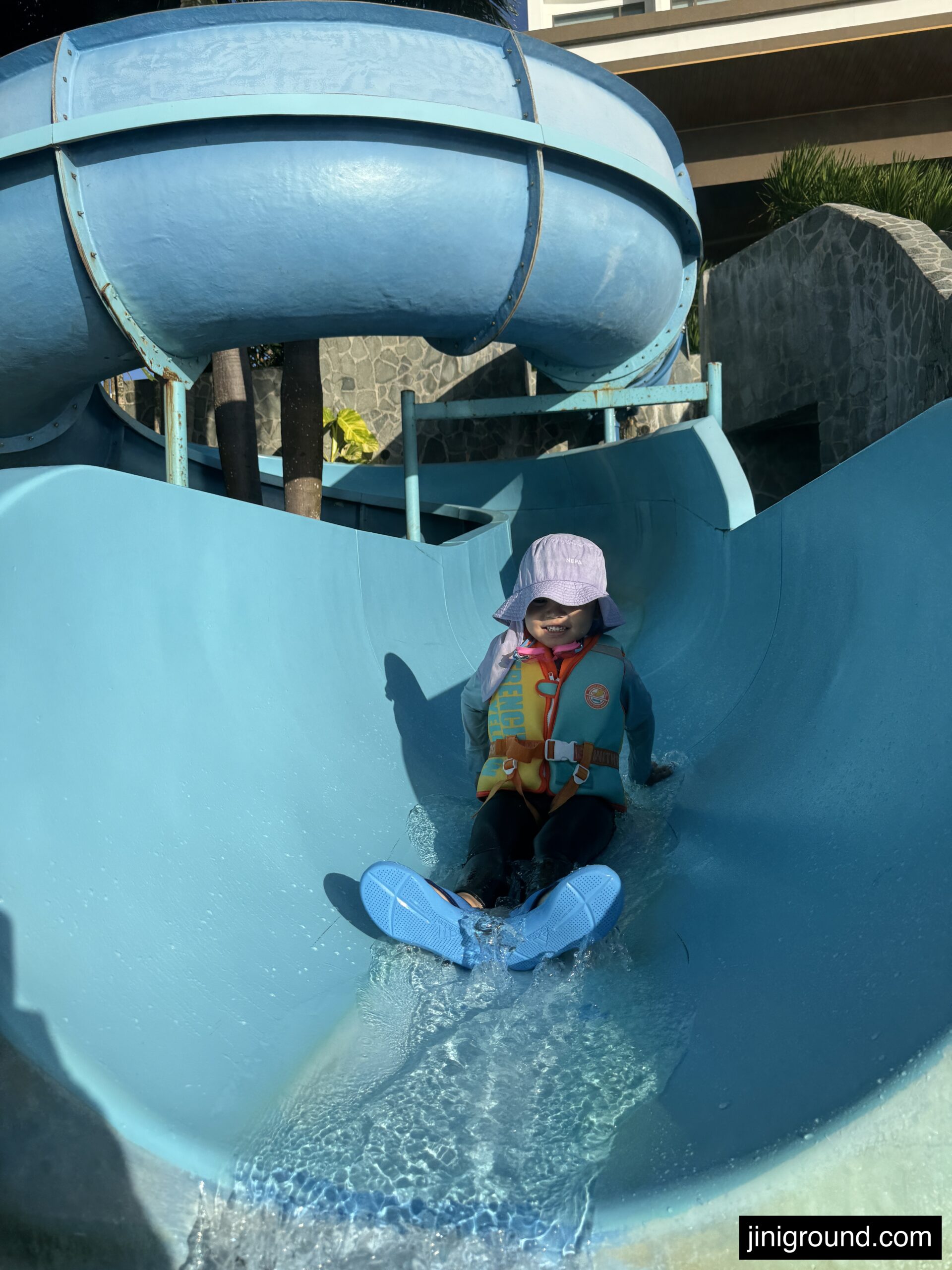 Boy sliding down blue water slide at Dusit Beach Resort pool area Guam