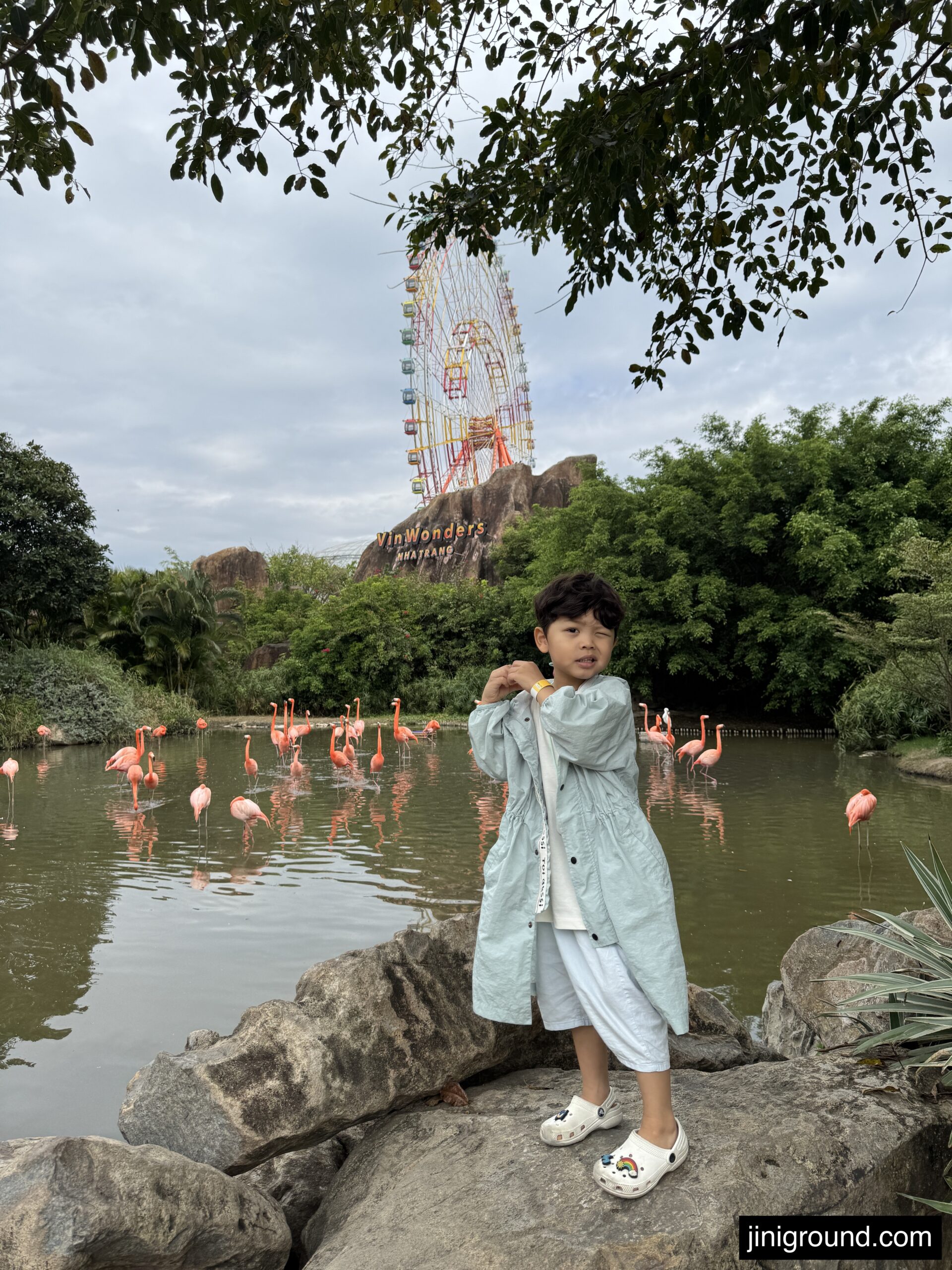 Boy sitting on rock with pink flamingos and ferris wheel in background at VinWonders Nha Trang