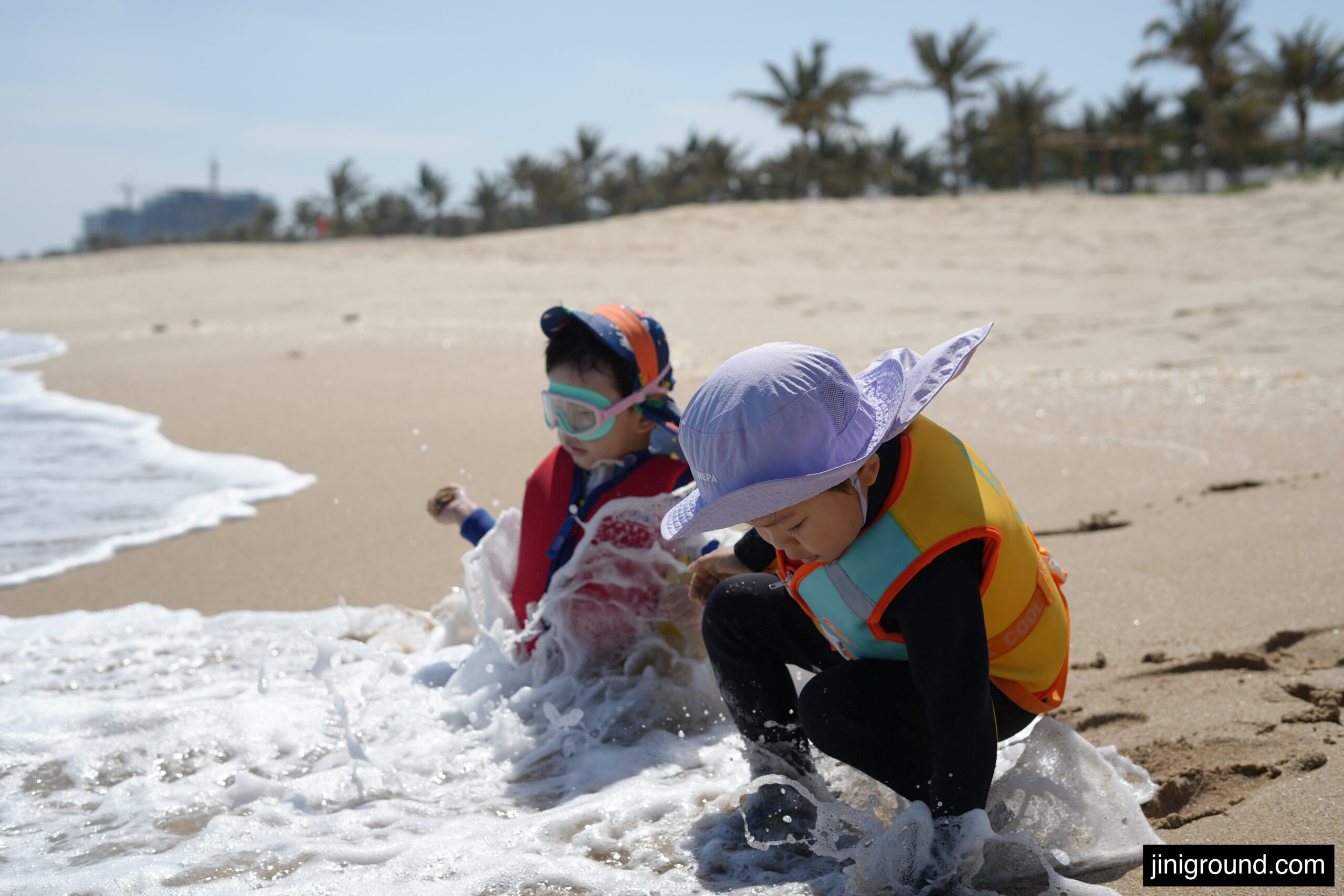 Two kids in life vests playing in ocean waves at Vinpearl Cam Ranh Beach Resort Nha Trang
