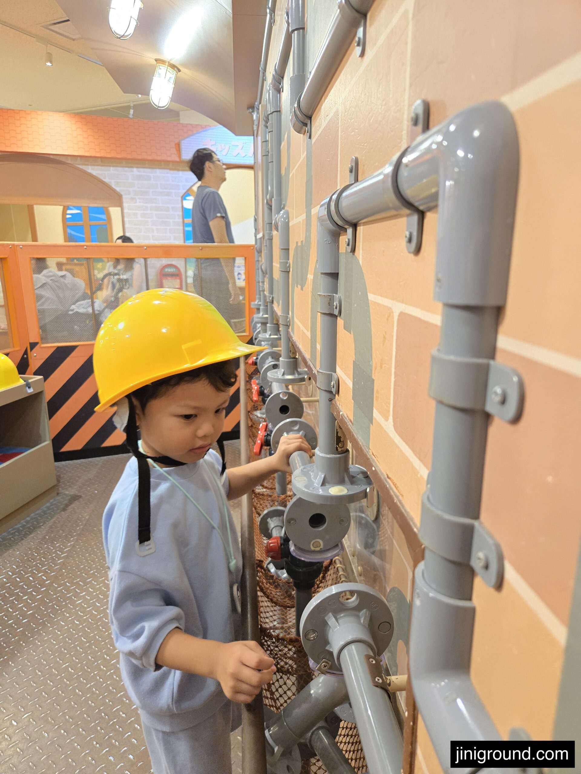 Young child wearing yellow hard hat exploring construction play area Osaka