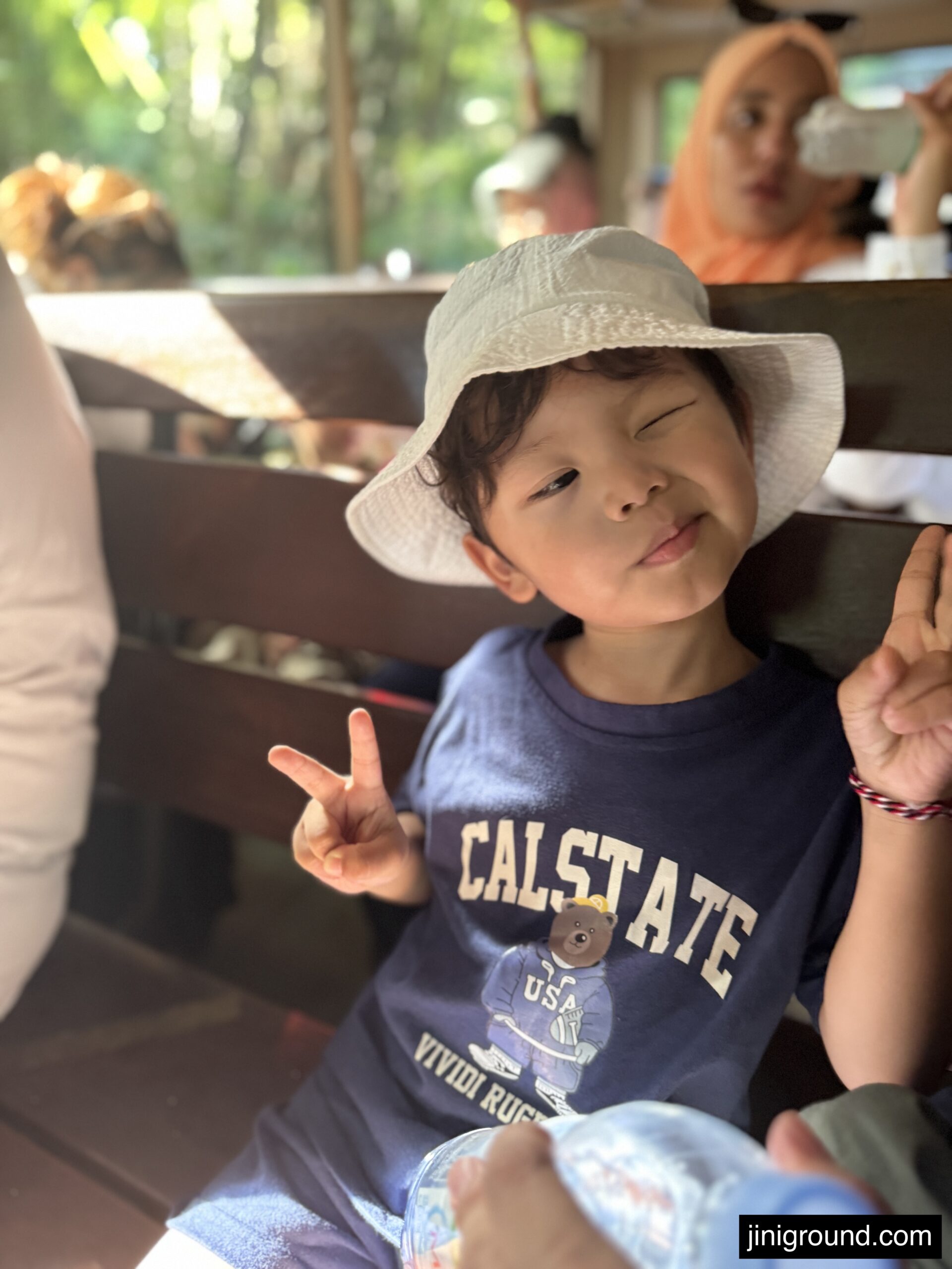 Young toddler wearing white sun hat making peace sign inside safari vehicle
