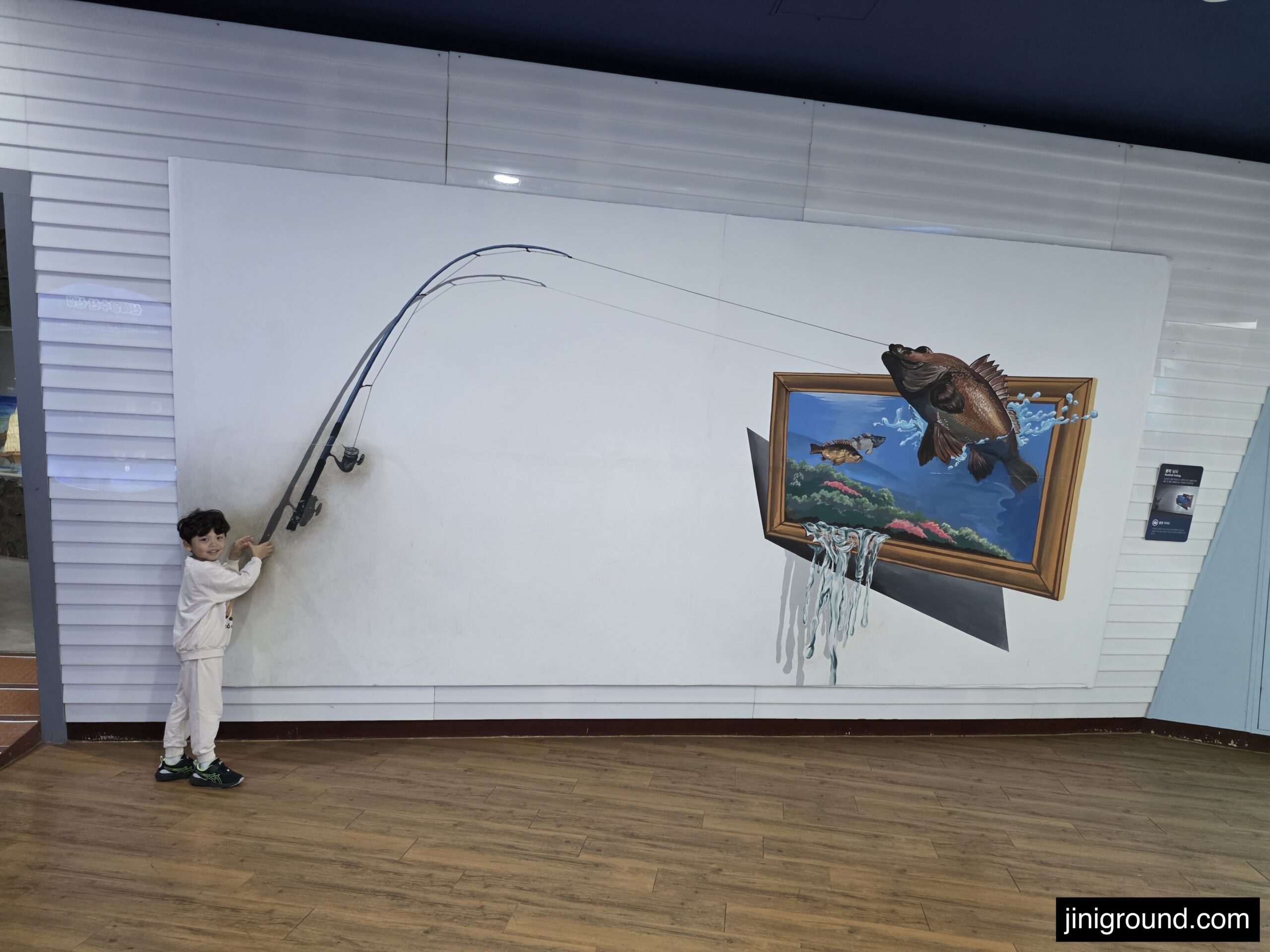 7-year-old boy posing with 3D fishing trick art mural at Tongyeong Marine Science Museum