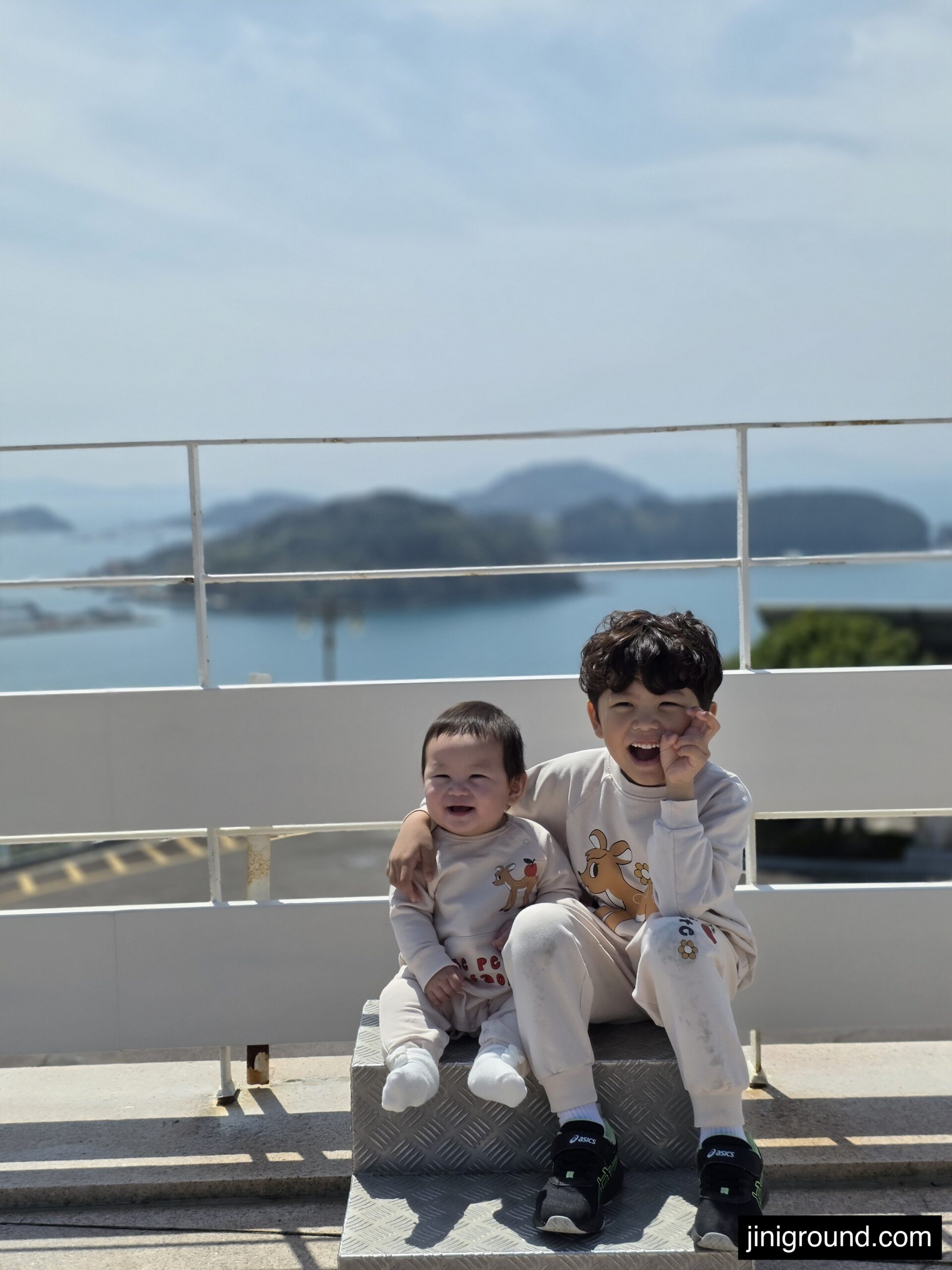 two brothers smiling together at Dara Park Tongyeong with beautiful sea and island view