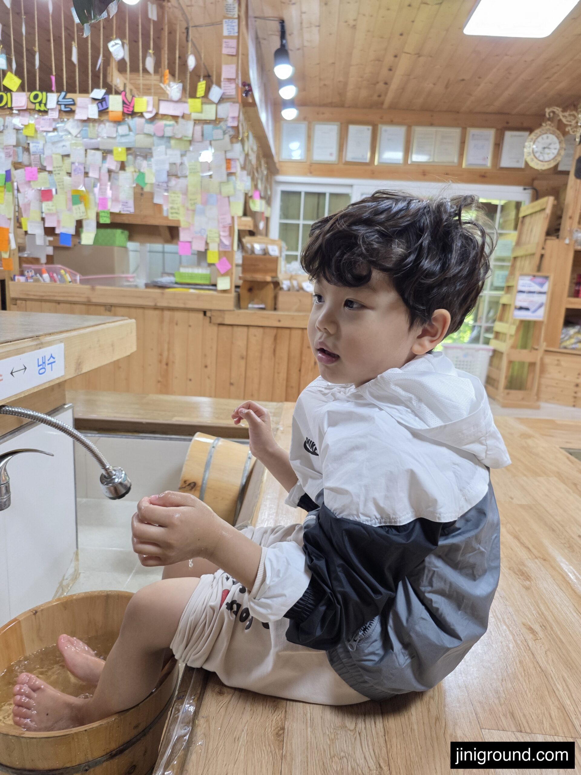 boy soaking feet in wooden barrel tub at Napoli Farm indoor facility with colorful memo notes on wall