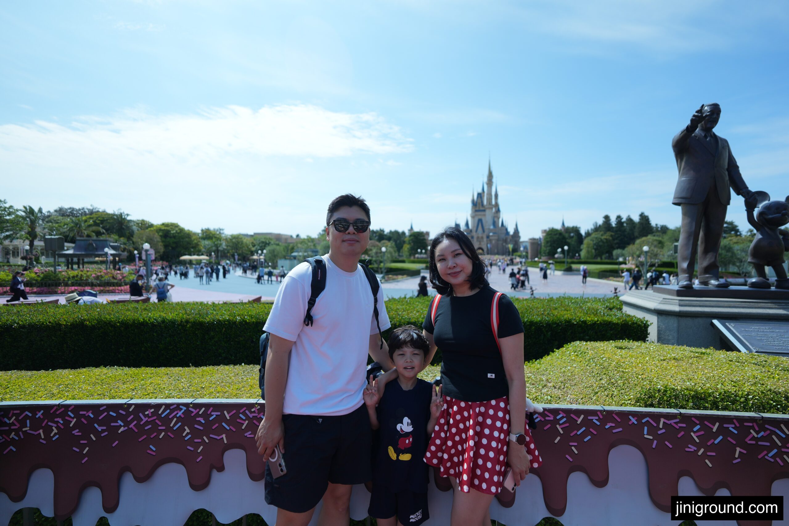 Family posing near Partners statue with Cinderella Castle at Tokyo Disneyland
