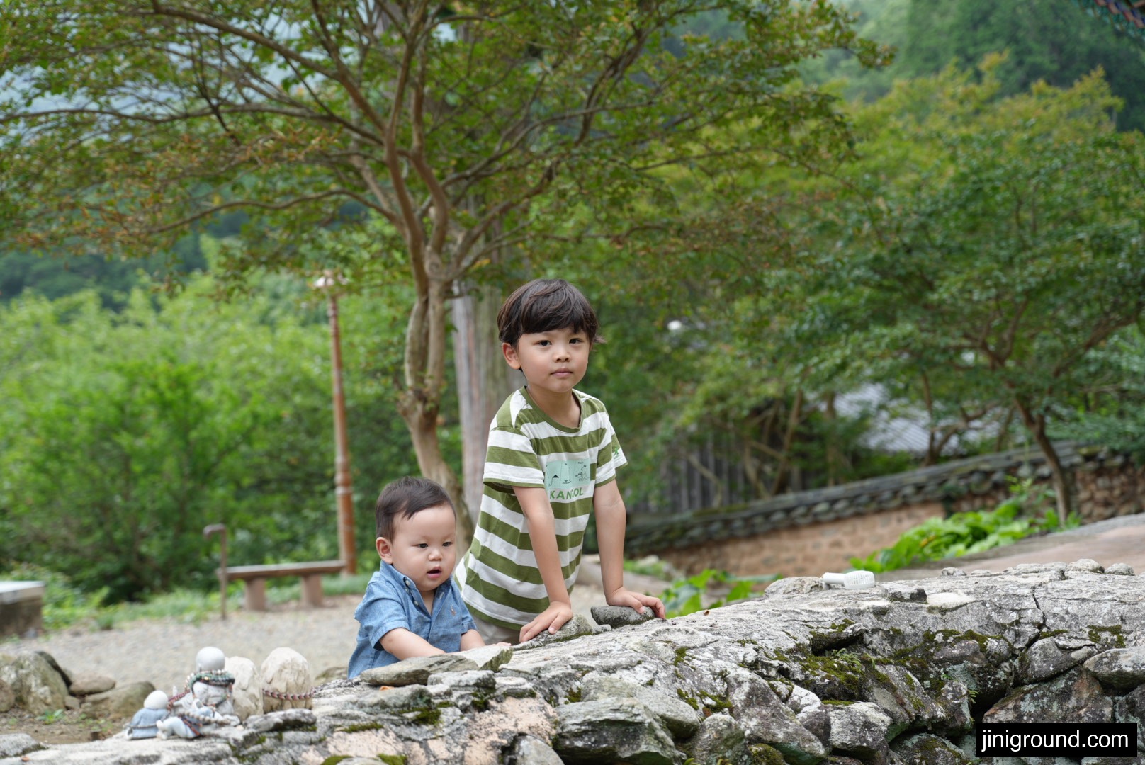 Two young siblings looking at small monk figurines on a stone wall at Seonamsa Temple
